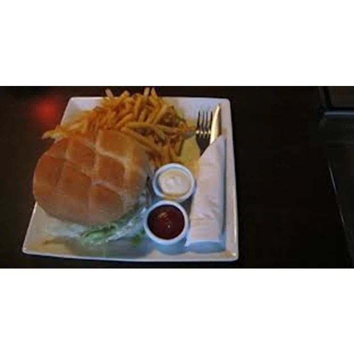 En tallerken med en burger, pommes frites, ketchup og mayonnaise ved siden af en sammenrullet serviet med gaffel og kniv på et mørkt bord.